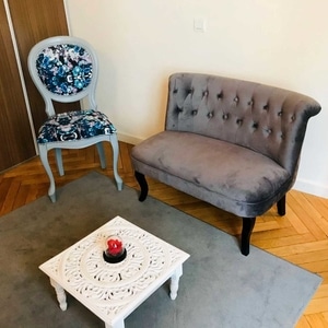 Petit salon avec banquette en velours gris, chaise médaillon fleurie et table basse blanche sculptée.