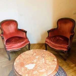Paire de fauteuils vintage en velours rouge et table basse ronde en marbre rose sur parquet.