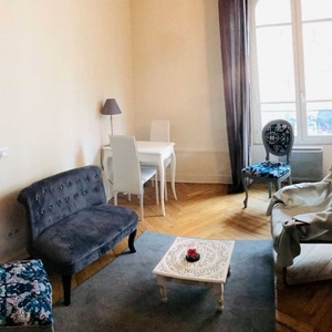 Salon avec canapé en velours gris, table basse blanche et coin repas lumineux sur parquet en chevrons.