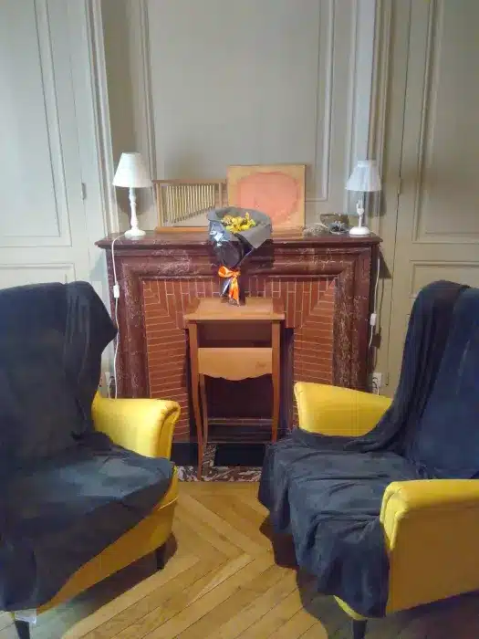 Salon chaleureux avec cheminée en brique, fauteuils jaunes et décoration soignée sur parquet en chevrons.