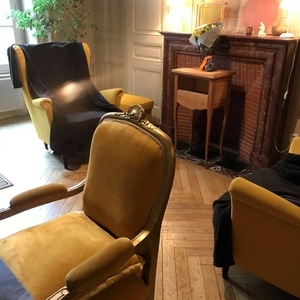 Salon chaleureux avec fauteuils en velours jaune, parquet en point de Hongrie et cheminée ancienne décorée.