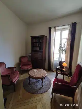 Salon classique avec fauteuils en velours rouge, table en marbre, bibliothèque en bois et parquet en chevrons.