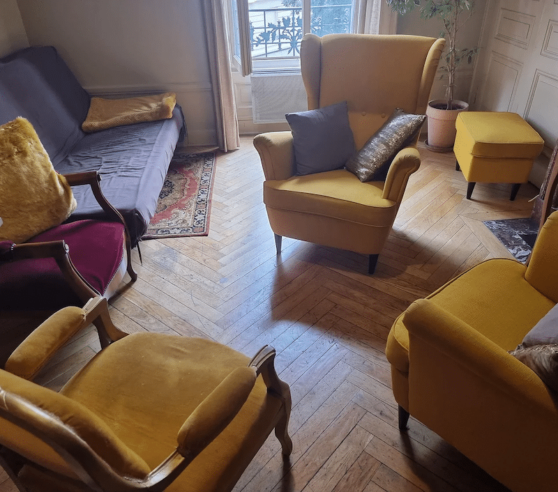 Salon élégant avec fauteuils jaune moutarde, canapé violet et sol en parquet point de Hongrie.