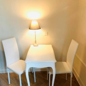 Table blanche galbée avec deux chaises blanches et lampe allumée dans un coin intérieur.